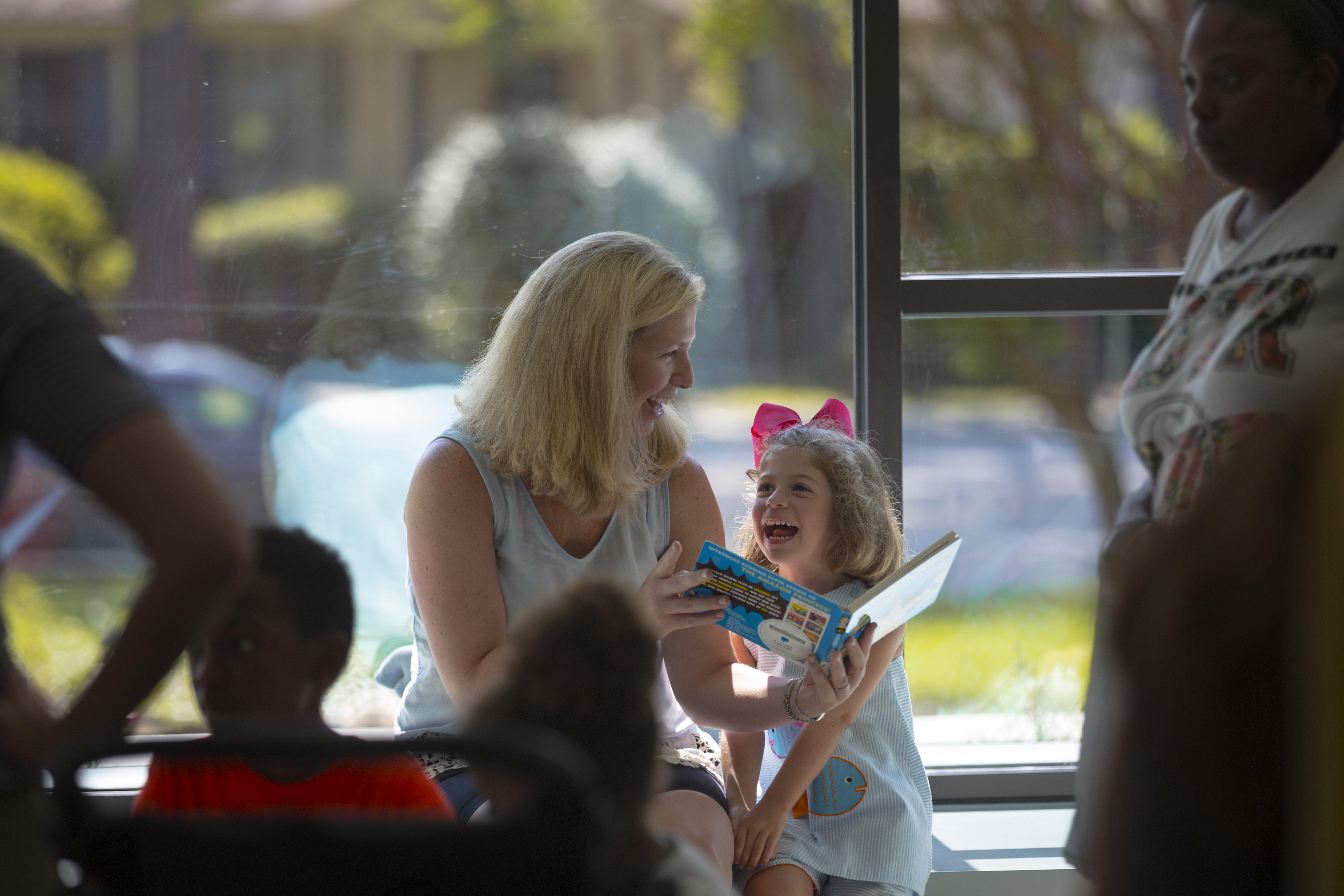 A White Mother and daughter read together in the window seat at Richland Library Cooper